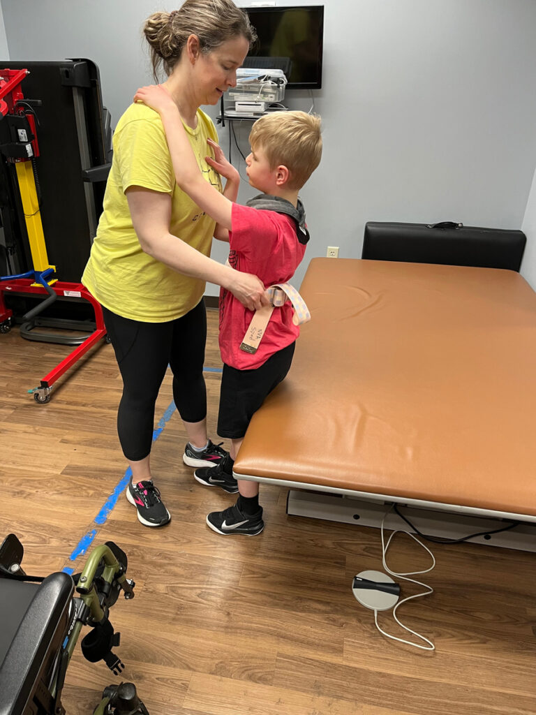 Caregiver lifting young boy while using assistive devices.