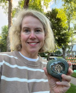 Sarah holding up a heart-shaped stone with the Family Achievement Foundation Logo on it
